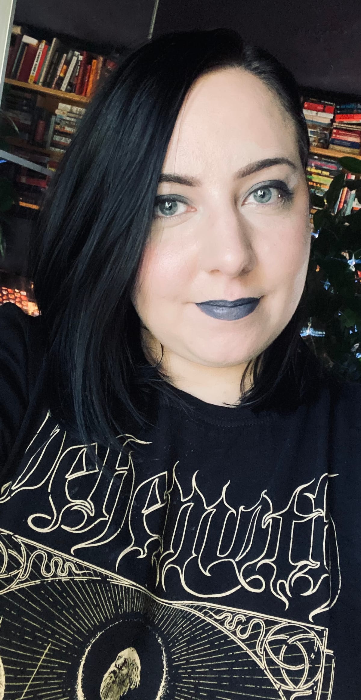 A selfie of me. I have jet black hair that falls to my shoulders and I am wearing smoky eyeshadow and gray lipstick. My black t-shirt has a logo on it for the band Behemoth.